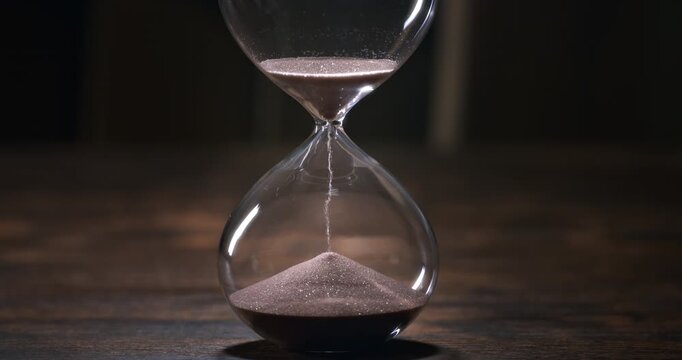 Hourglass with sand falling in super slow motion, evoking the passage of time, mortality, patience and the fleeting nature of life.
