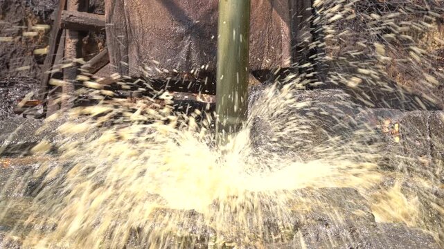 Traditional crude oil extraction using a pipe bailer at Teksas Wonocolo traditional oil field in Bojonegoro, East Java, Indonesia. Manual petroleum mining process from deep well with raw oil splash.