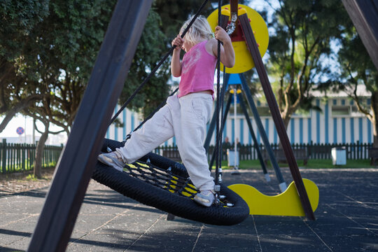 Carefree Little Girl Balancing and Playing on Web Nest Swing at Outdoor Playground