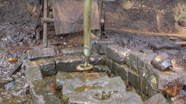 Traditional crude oil extraction using a pipe bailer at Teksas Wonocolo traditional oil field in Bojonegoro, East Java, Indonesia. Manual petroleum mining process from deep well with raw oil splash.