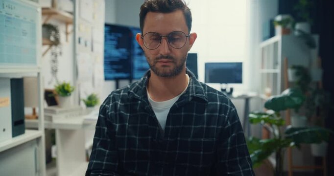 Young Caucasian male programmer writes code using multiple screens in home office workspace. AI development, cybersecurity, network database system, software engineering, remote tech startup concept.