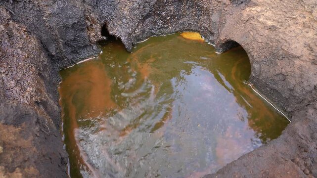 Crude oil flows into an open containment pit at Teksas Wonocolo traditional oil mining field, Bojonegoro, East Java, Indonesia, showing raw petroleum extraction and industrial environmental impact.