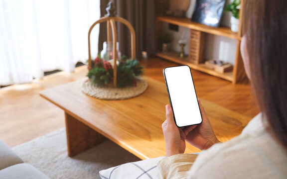 Mockup image of a woman holding and using mobile phone with blank desktop white screen at home