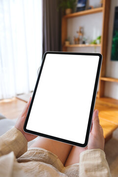 Vertical mockup image of a woman holding tablet with blank desktop white screen at home