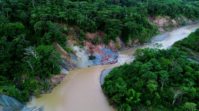 Aerial view of a landslide exposing colourful soil and rock beside river surrounded by tropical rainforest, Illustrating erosion, slope instability, geological hazards and ecosystem disturbance.