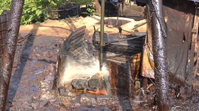 Traditional crude oil extraction using a pipe bailer at Teksas Wonocolo traditional oil field in Bojonegoro, East Java, Indonesia. Manual petroleum mining process from deep well with raw oil splash.