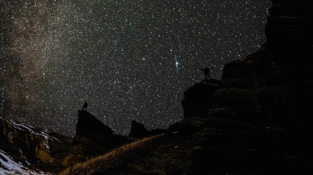 Two travelers on mountain cliffs looking at a starry night sky and Milky Way Galaxy timelapse