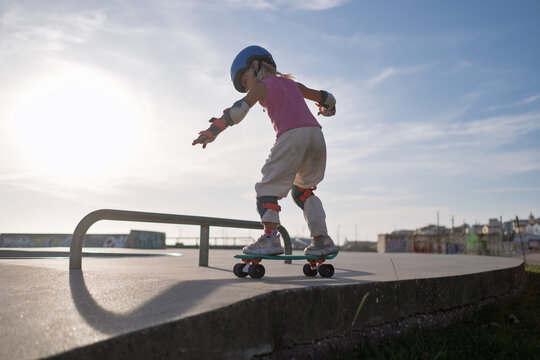 Little Girl in Helmet and Protective Gear Balancing on Penny Board at Skatepark