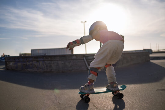 Little Girl in Helmet and Protective Gear Balancing on Penny Board at Skatepark