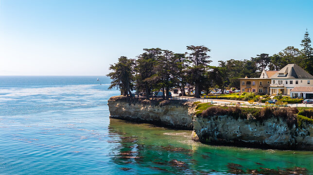 Aerial view shows the sandstone cliffs along West Cliff Drive in Santa Cruz, California, featuring coastal cypress trees, seaside homes, and kelp beds in the Pacific ocean.