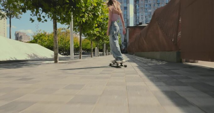 Tracking camera follows young woman longboarding through sunny urban passage with relaxed confident energy. City recreation, youth freedom and active lifestyle concept.