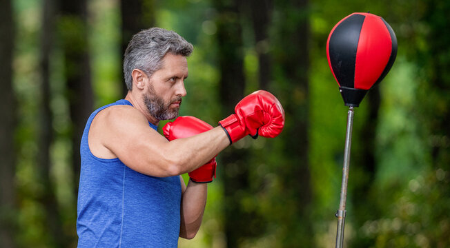 Strong athlete man. Sportsman punching bag. Boxer with punching bag. Exercising and punching. Practicing boxing. Sportsman in boxing gloves outdoor. Strong man. Active lifestyle. Sport man boxing