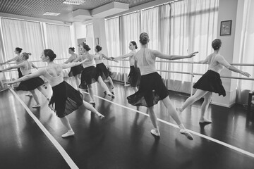Female ballet dancers practicing arabesque in studio under soft monochrome light