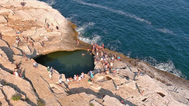 Aerial view of Giola natural pool with people swimming in the turquoise water surrounded by rocky cliffs in Thasos, Greece.