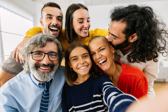 Joyful multigenerational family taking selfie together at home. Happy caucasian people of different ages smiling at camera, hugging in living room. Technology and family concept.