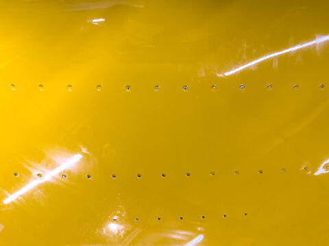 Close-up of bright yellow metal machine with many small holes and rivets
