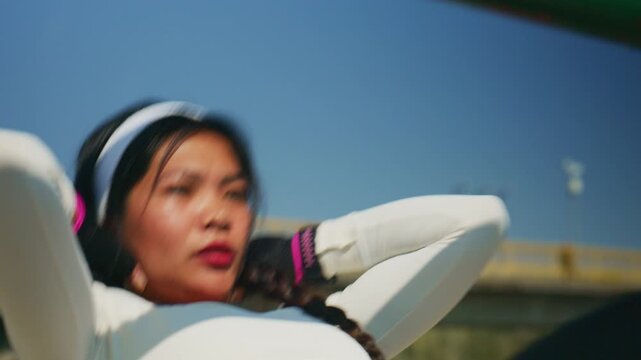 An Asian woman performs sit-ups on an outdoor horizontal bar, building core strength. She focuses on her fitness with a challenging workout.