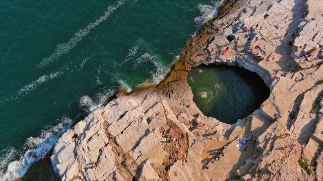 Aerial view of the Giola natural pool with people swimming in the turquoise water surrounded by rocky cliffs on the coast of Thasos, Greece.