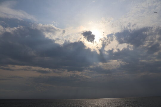 Evening sun casting a warm glow through the clouds over a calm bay.