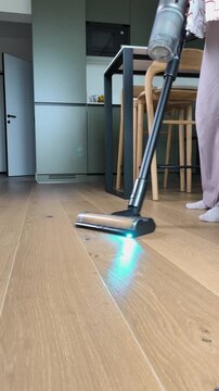 Backlit vacuum cleaner nozzle moving on parquet flooring for effective apartment dust removal. Modern house chore process with wireless stick vacuum cleaning tool in light living room.