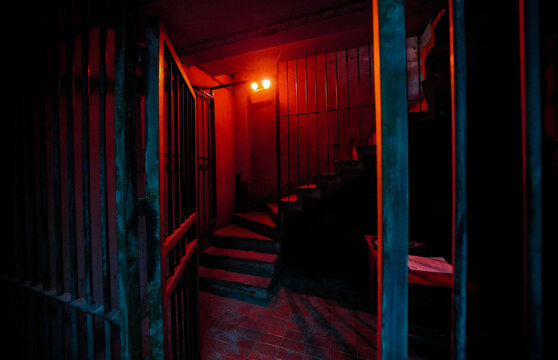 View Through Iron Bars of Dark Prison Cell with Open Gate and Red Light