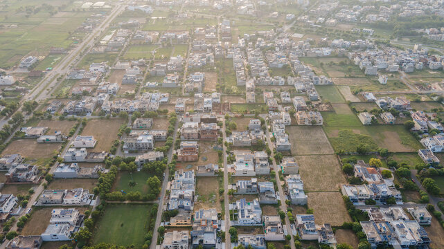 Aerial view of a residential neighborhood in Lahore featuring houses with rooftops, solar panels, and surrounding green spaces in Lahore, Punjab, Pakistan.
