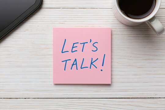Note with pink sticky paper message lets talk on wooden office desk near white coffee cup
