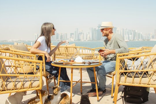 Happy travel couple sit in cafe on vacation eat snack enjoy together man adult carefree get away trip. Doha qatar waterfront outdoors cafe popular scenic viewpoint.Couple vacation holidays middle east