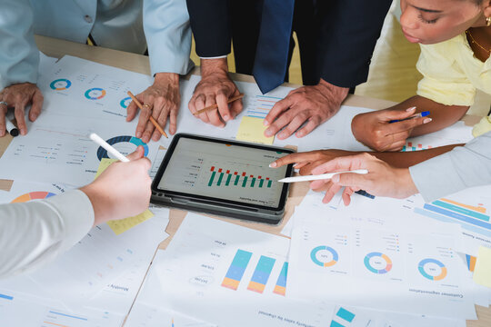 overhead view of a business team analyzing charts and data spread across a table, with a tablet displaying a SWOT analysis. This detailed shot captures strategic planning, collaboration, and data-driv