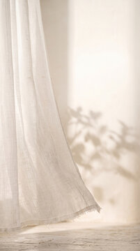 Sheer cream-white linen curtain with a lifted frayed hem above a sunlit floor, botanical shadows, and luminous ivory plaster