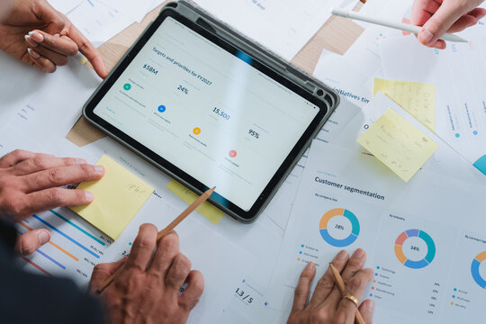 overhead view of a business team analyzing charts and data spread across a table, with a tablet displaying a SWOT analysis. This detailed shot captures strategic planning, collaboration, and data-driv