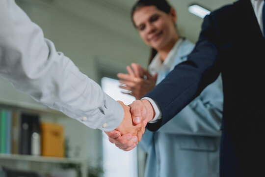 closeup of two businessmen shaking hands, with a colleague applauding softly out of focus behind them. This detailed shot captures trust, agreement, and celebratory success in a professional office se