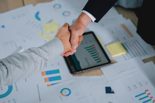 closeup of two businessmen shaking hands, with a colleague applauding softly out of focus behind them. This detailed shot captures trust, agreement, and celebratory success in a professional office se