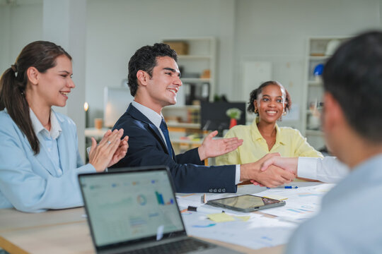 diverse team collaborates during a business meeting, smiling and engaged around a laptop displaying data charts. This candid office moment captures teamwork, professionalism, and positive workplace co