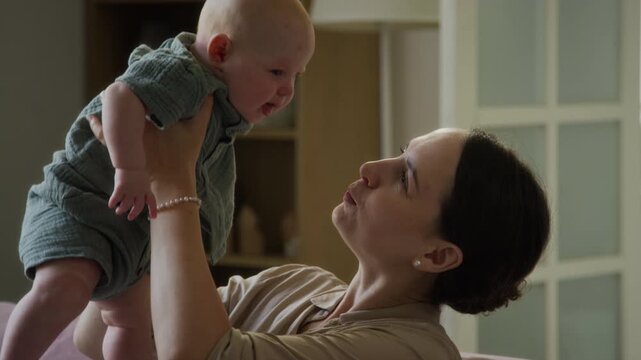 Caucasian mother smiling, lifting and kissing infant indoors. Clip suitable for parenting campaigns, maternal health advertising and family insurance commercials