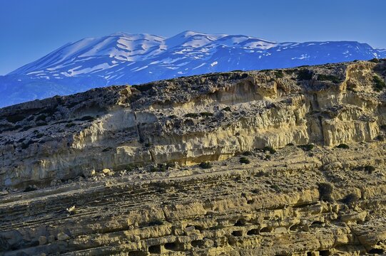 Neolithic caves, former hippie paradise, eroded, layered rock formation in front of snow-capped mountains under blue sky, Matala, south coast, Crete, Greek Islands, Greece