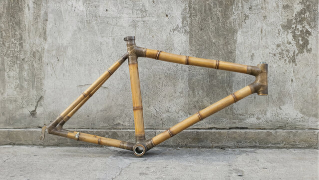 Handmade bamboo bicycle frame leaning against a textured concrete wall in urban setting