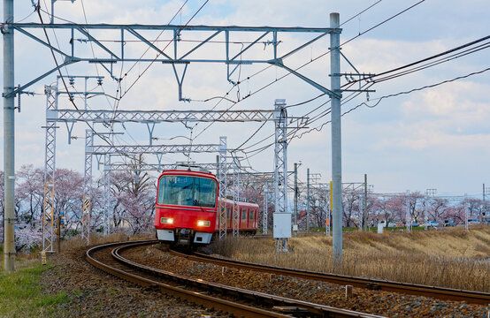 A rapid train of Meitetsu Nagoya Main Line traveling through a railway curve and beautiful cherry blossom trees (Sakura) along the tracks blooming on a sunny spring day, in Kasamatsu, Gifu, Japan