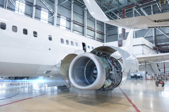 White passenger airplane with open high bypass turbofan aircraft engine in aviation hangar. Checking mechanical systems for flight operations