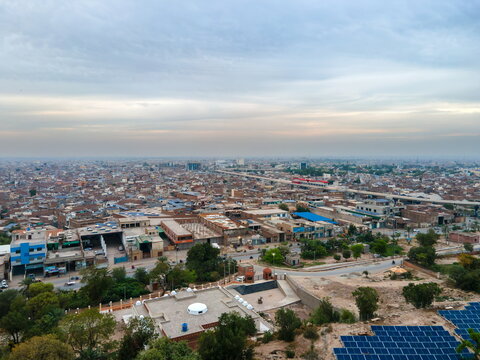 Aerial view of the urban landscape featuring residential and commercial buildings, a solar panel array in the foreground, and a hazy sky in Multan, Punjab, Pakistan.