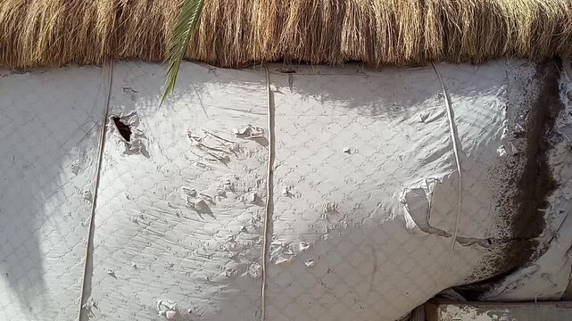 Worn fabric wall of beach bungalow under thatched straw roof