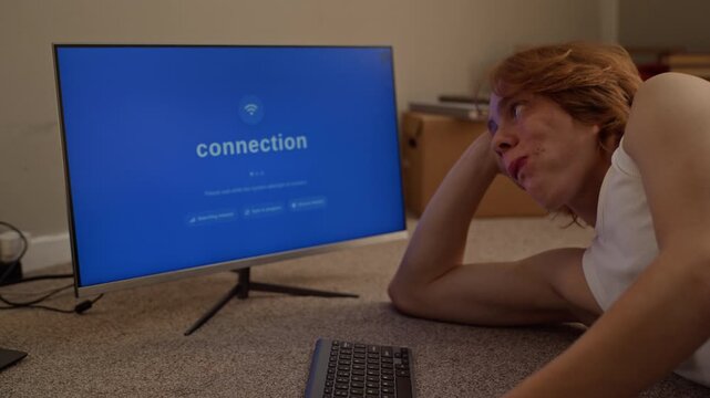 Caucasian young man lying on floor eating fast food while waiting for slow internet connection on monitor. Footage suitable for network outage campaigns and telecom advertisements