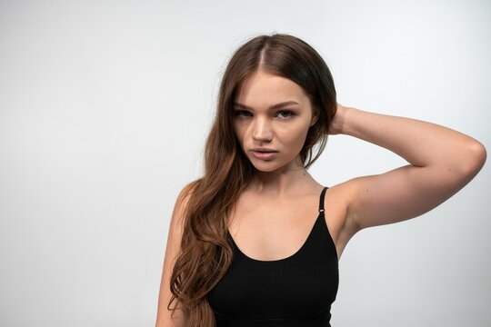 Young woman posing in a black tank top, touching her long hair. Studio shot on a clean white background