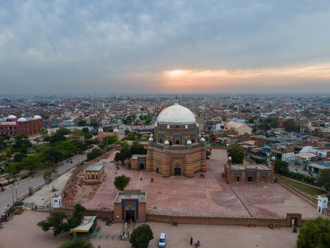 Aerial view of the historic Tomb of Shah Rukn-e-Alam with its large white dome and brickwork, set amidst the urban landscape of Multan during a golden sunset in Multan, Punjab, Pakistan.