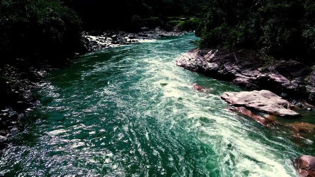 Aerial view following a fast turquoise river through smooth exposed rock and dense tropical vegetation. Swirling currents create a vivid wilderness scene associated with freshwater ecology, adventure 
