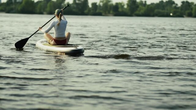 Paddleboarder Paddling On Sup Board Sitting On Water On River During. Active Recreation In Summer 