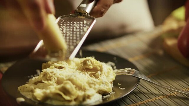 Chef Grating Fresh Parmesan Cheese Over Hot Ravioli Pasta On Plate With Metal Grater. Preparing Homemade Italian Meal