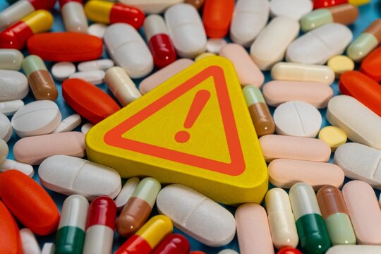 Warning sign with a red exclamation mark and a colorful medical pills. Drug safety, medication side effects, overdose risks, and pharmaceutical contraindications concept.