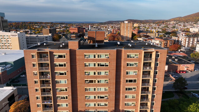 Aerial view of a multi-story brick residential building with balconies, surrounded by the urban cityscape of Reading during autumn, Reading, Pennsylvania, United States.