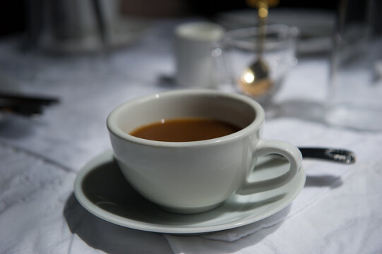View of a white ceramic coffee cup on a saucer placed on a white tablecloth in Point Roberts, Washington, United States.